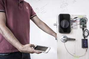 UW engineers use a smartphone to send a secure password through the human body and open a door with an electronic smart lock. These “on body” transmissions employ low-frequency signals generated by the phone’s fingerprint sensor. Photo credit: Mark Stone/University of Washington